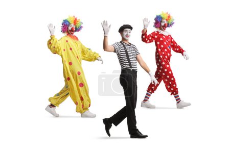 Téléchargez les photos : Plan complet de deux clowns et d'un mime marchant et agitant isolé sur fond blanc - en image libre de droit