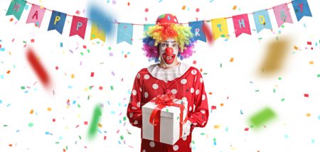 Téléchargez les photos : Clown avec un cadeau d'anniversaire et confettis autour isolé sur fond blanc - en image libre de droit