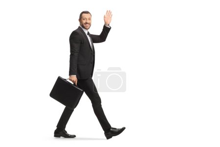 Photo for Full length shot of a businessman walking with a briefcase and waving isolated on white background - Royalty Free Image