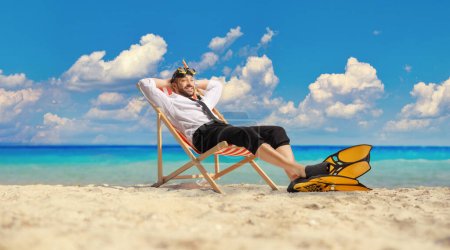 Téléchargez les photos : Homme d'affaires avec palmes de plongée et masque assis sur une chaise bech au bord de la mer - en image libre de droit