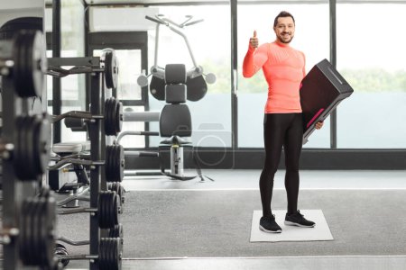 Photo for Man with a step aerobic platform showing thumb up at the gym - Royalty Free Image