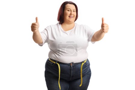 Photo for Cheerful corpulent woman in jeans with a measuring tape around waist gesturing thumbs up isolated on white background - Royalty Free Image