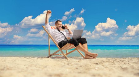 Photo for Happy bussinesman on a beach chair using a laptop and a smartphone by the sea - Royalty Free Image