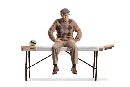 Foto de Hombre mayor sentado en una cama de fisioterapia aislado sobre fondo blanco - Imagen libre de derechos