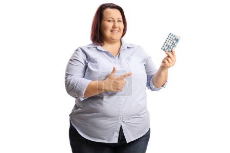 Foto de Mujer con sobrepeso sosteniendo un paquete de pastillas y señalando aislado sobre fondo blanco - Imagen libre de derechos