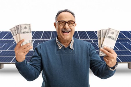 Foto de Emocionado hombre maduro sosteniéndonos dólares frente a un campo fotovoltaico aislado sobre fondo blanco - Imagen libre de derechos