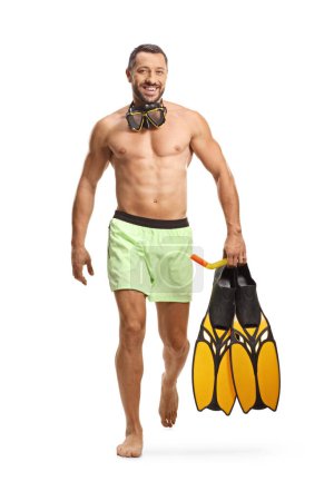 Téléchargez les photos : Portrait complet d'un jeune homme en maillot de bain avec un masque de plongée tenant des palmes de plongée et marchant isolé sur fond blanc - en image libre de droit