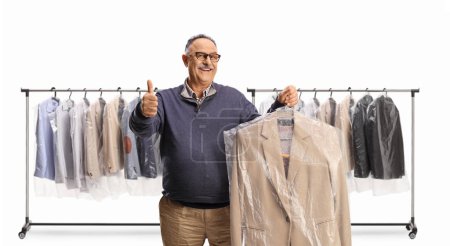 Photo for Mature man collecting a suit from dry cleaners and gesturing thumbs up isolated on a white backgroun - Royalty Free Image