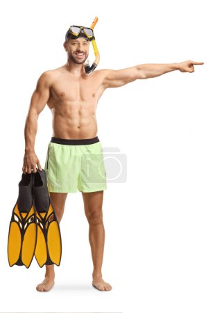 Photo for Full length portrait of a young man in swimwear with a diving mask holding snorkeling fins and pointing isolated on white background - Royalty Free Image