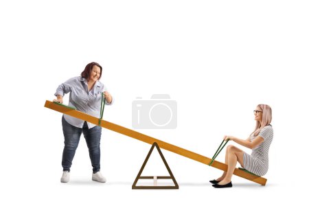 Photo for Overweight woman lifting a thin woman on a seesaw isolated on white background - Royalty Free Image