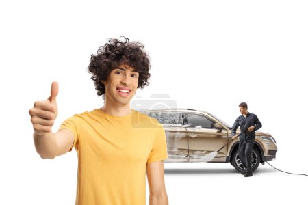 Téléchargez les photos : Joyeux jeune homme avec un SUV geste pouce vers le haut signe à un lavage de voiture isolé sur fond blanc - en image libre de droit