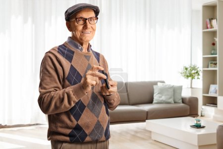 Foto de Elderly man poking finger with an insulin pen at home in a living room and smiling - Imagen libre de derechos