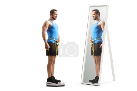 Photo for Full length shot of a fit man in sportswear measuring waist and standing on a weight scale in front of a mirror isolated on white background - Royalty Free Image