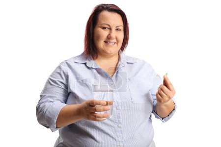 Foto de Overweight woman holding a glass of water and a pill isolated on white backgroun - Imagen libre de derechos