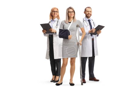 Téléchargez les photos : Doctors standing behind a young female patient with an arm sling and a crutch isolated on white background - en image libre de droit