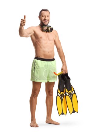 Photo for Fit man in swimwear with a diving mask and snorkeling fins gesturing thumbs up isolated on white background - Royalty Free Image