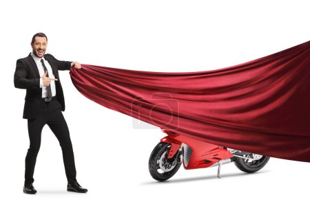 Photo for Businessman pulling a red piece of cloth and pointing at a motorbike isolated on white background - Royalty Free Image