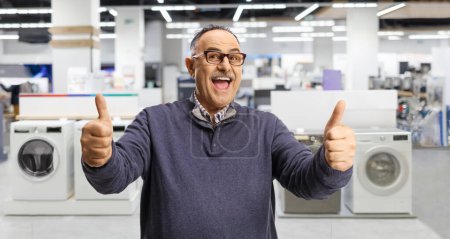 Photo for Excited mature man gesturing thumbs up inside an appliance store - Royalty Free Image