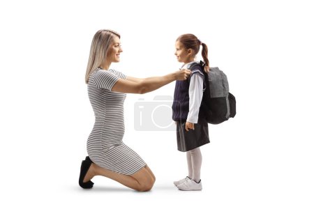 Foto de Full length profile shot of a mother helping a daughter to get ready for school with a backpack isolated on white background - Imagen libre de derechos
