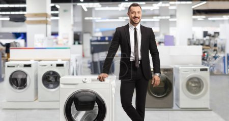 Téléchargez les photos : Man in a suit leaning on a washing machine inside a shop - en image libre de droit