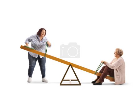 Téléchargez les photos : Overweight woman lifting an elderly woman on a seesaw isolated on white background - en image libre de droit