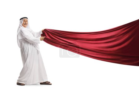 Foto de Hombre árabe con ropa tradicional tirando de un trozo de tela roja aislada sobre fondo blanco - Imagen libre de derechos