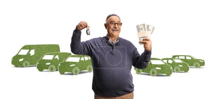 Foto de Hombre maduro sonriente sosteniendo una llave de coche y montones de dinero frente a vehículos eléctricos verdes aislados sobre fondo blanco - Imagen libre de derechos