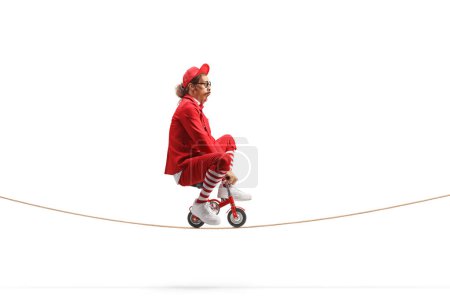 Téléchargez les photos : Homme en costume rouge sur un petit vélo rouge sur une corde isolée sur fond blanc - en image libre de droit