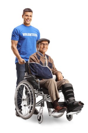 Téléchargez les photos : Volontaire aidant un homme âgé blessé avec une attelle de jambe dans un fauteuil roulant isolé sur fond blanc - en image libre de droit