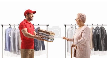 Foto de Trabajador masculino entregando una pila de ropa doblada de la tintorería a una anciana aislada sobre un fondo blanco - Imagen libre de derechos
