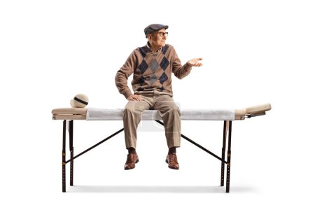 Foto de Anciano sentado en una cama de fisioterapia y haciendo gestos con la mano aislada sobre fondo blanco - Imagen libre de derechos