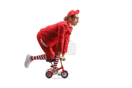 Photo for Funny entertainer in a red suit riding a small bike isolated on white background - Royalty Free Image