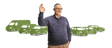 Téléchargez les photos : Gai mature homme gestuelle ok signe en face de verts véhicules électriques isolés sur fond blanc - en image libre de droit