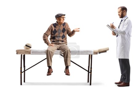 Foto de Hombre mayor sentado en una cama de fisioterapia y hablando con un médico aislado sobre fondo blanco - Imagen libre de derechos