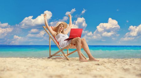 Téléchargez les photos : Belle jeune femme en robe blanche assise sur la plage avec un ordinateur portable - en image libre de droit