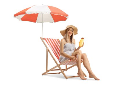 Téléchargez les photos : Femme assise sur une chaise longue et appliquant de la crème solaire sur les jambes isolées sur fond blanc - en image libre de droit