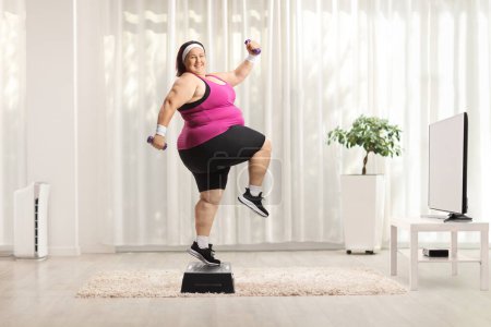 Foto de Mujer con sobrepeso haciendo ejercicio aeróbicos paso en casa delante de la televisión - Imagen libre de derechos