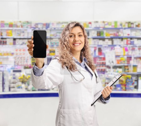 Foto de Farmacéutico con un documento en un portapapeles que muestra un smartphone en una farmacia - Imagen libre de derechos