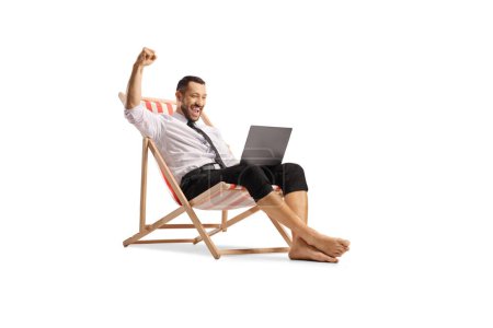 Téléchargez les photos : Homme d'affaires profiter sur une chaise de plage avec un ordinateur portable et geste victoire isolé sur fond blanc - en image libre de droit