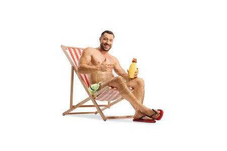 Photo for Young man holding a bottle of sun cream seated at a beach chair isolated on white background - Royalty Free Image