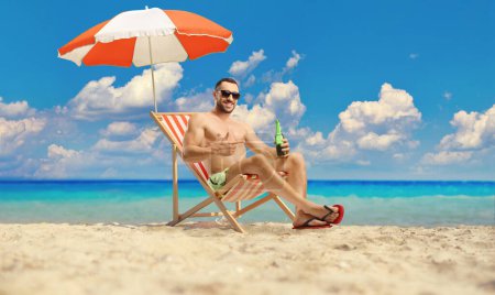 Photo for Man at the beach sitting under umbrella with a bottle of cold beer - Royalty Free Image