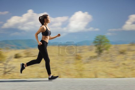 Photo for Full length profile shot of a young female jogging on a road - Royalty Free Image