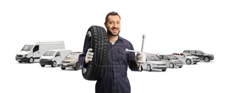 Photo for Auto mechanic holding a tire on his shoulder and a lug wrench in front of many vehicles isolated on white background - Royalty Free Image