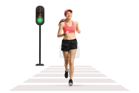 Photo for Full length portrait of a young smiling woman in sportswear jogging on a street at pedestrian crosswalk isolated on white background - Royalty Free Image