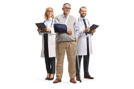Téléchargez les photos : Homme mûr avec des béquilles et un bras blessé debout devant des médecins isolés sur fond blanc - en image libre de droit