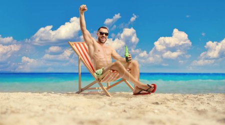 Photo for Man at the beach by the sea holding a bottle of beer and gesturing happiness - Royalty Free Image