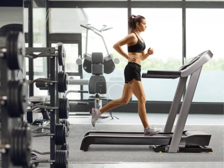 Photo for Full length profile shot of a fit young female running on a treadmill in a gym - Royalty Free Image