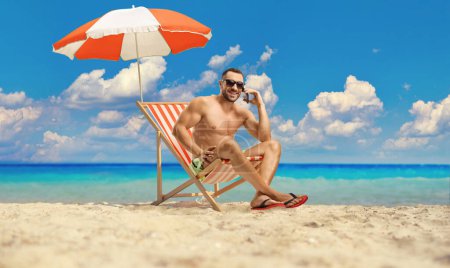 Photo for Young man at the beach under umbrella using a smartphone - Royalty Free Image