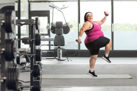 Photo for Cheerful overweight woman exercising with weights at the gym - Royalty Free Image