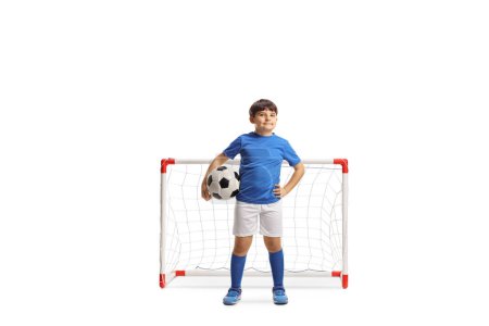 Photo for Full length portrait of a boy in sports jersey holding a soccer ball and posing in front of a mini goal isolated on white background - Royalty Free Image